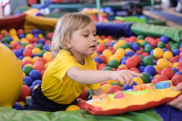 Retrato de um rapaz louro com uma t-shirt amarela. A criança sorri e brinca na sala de jogos das crianças. Bola piscina . — Fotografia de Stock