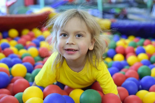 Retrato de um rapaz louro com uma t-shirt amarela. A criança sorri e brinca na sala de jogos das crianças. Bola piscina . — Fotografia de Stock