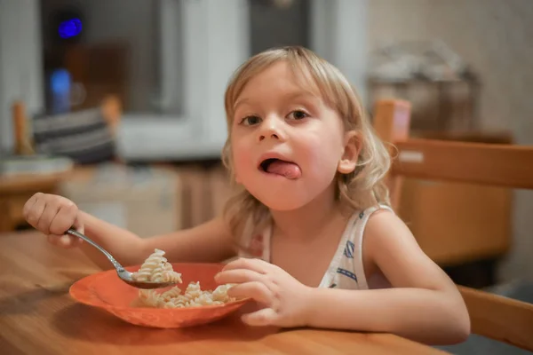 Bambino carino 4 anni seduto e mangiare da solo in cucina. Ritratto di un ragazzo biondo. Il bambino sorride e mangia la pasta. Buon appetito, dieta sana . — Foto Stock