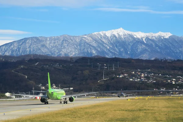 Adler, Oroszország. Utazási. Repülőtér nézet. Sochi nemzetközi repülőtér. Zöld fű között kifutópályán és gyönyörű hegyek a háttérben. — Stock Fotó