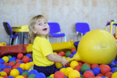 Sarı tişört sarışın bir çocuk portresi. Çocuk gülümsüyor ve çocuk odasında oynuyor. Top Havuzu.