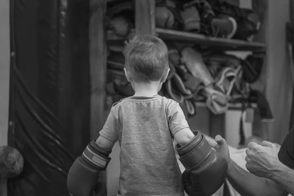 Yüzük üzerinde boks eldivenleri olan küçük çocuk. Çocuk boks eğitim Punch mitts egzersiz kavramı. Arkaya bakın. siyah ve beyaz. — Stok fotoğraf