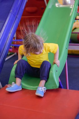Tepeye binen bir çocuk. Sarı tişörtlü sarışın bir çocuğun portresi. Çocuk gülümsüyor ve çocuk oyun odasında oynuyor.