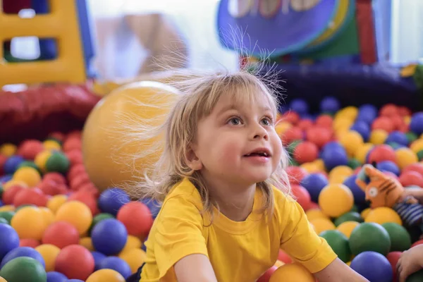A szőke fiú, egy sárga pólót portréja. A gyermek mosolyog és játszik a játszószobában. Golyós pool. — Stock Fotó