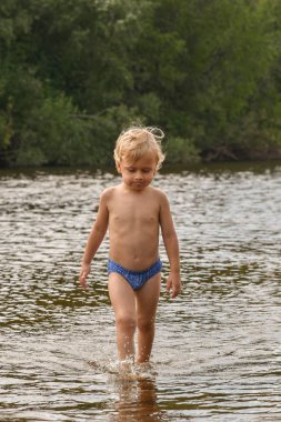 Bebek çocuk yalınayak suda sahilde yürüyor. İyi havalarda nehirde yaz aylarında tatilde çocuk.