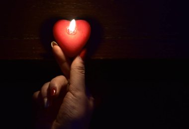 Karanlık ışık yanan kırmızı mum tutan kadın el. Sevgililer günü hediyesi. Romantizm