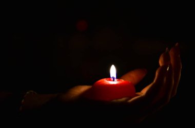 Kırmızı yanan mum bir kadın eli karanlıkta yatarken. Sevgililer günü hediyesi.