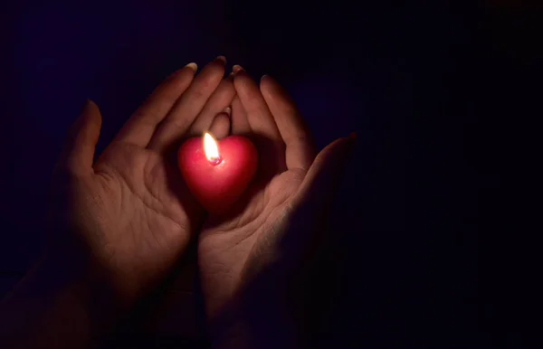 Women's hand holding a burning red candle in the dark light.Valentine's day gift. romance