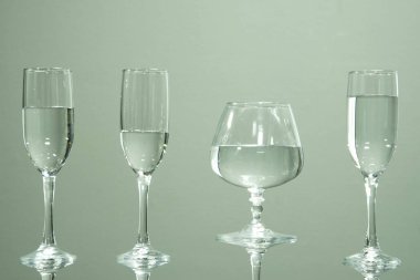 Bir tabloda, gri bir arka plan üzerinde duran su ile dolu dört camlar.