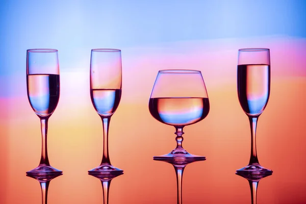 Четыре бокала вина воды на столе, за красочным фоном. Очки отражаются в стакане . — стоковое фото
