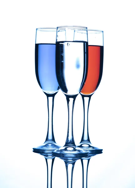 Три бокала шампанского, с жидкостью разных цветов, на голубом фоне . — стоковое фото