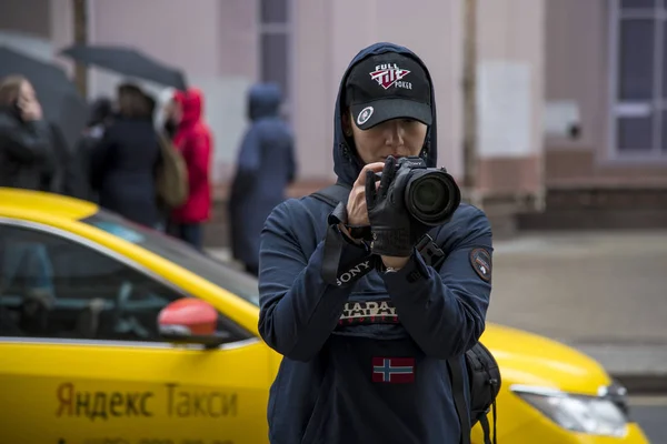 Április 2019, Moszkva, Oroszország. Lány fotós sötét ruhát és baseball sapka fényképeket az utcán, nedves időben — Stock Fotó