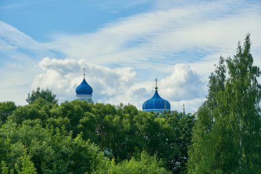 Ağaçların arkasında mavi bulutlu gökyüzüne karşı Kilisenin parlak mavi kubbeleri vardır..