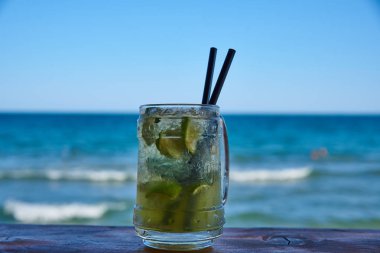 İki siyah tüpler ile barda bir buharda Mojito bardak. Deniz ve mavi gökyüzüne karşı.