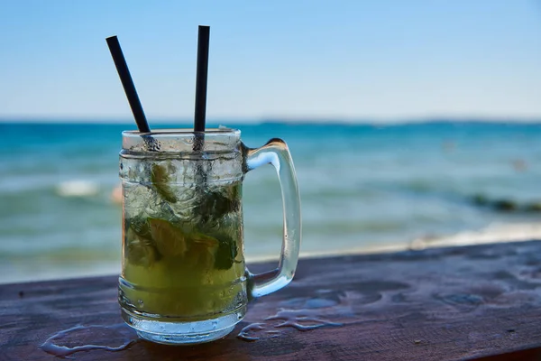 A steamed glass of Mojito on the bar with two black tubes.Against the sea and blue sky.