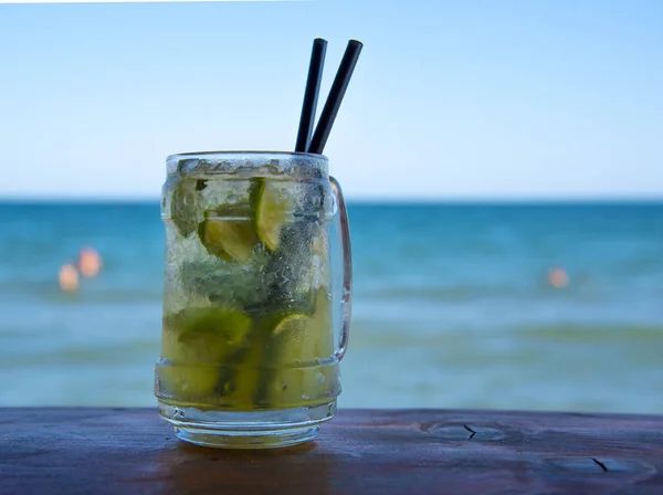 A steamed glass of Mojito on the bar with two black tubes.Against the sea and blue sky.