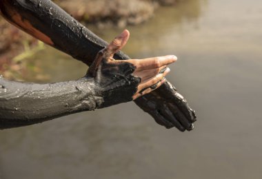 Eller siyah şifa çamuriçinde. Bir el diğerini lekeler..
