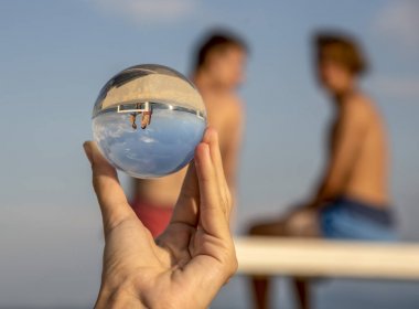 Ön planda, bir el bulanık bir arka plan üzerinde oturan iki genç yansıtan bir lens topu tutar.