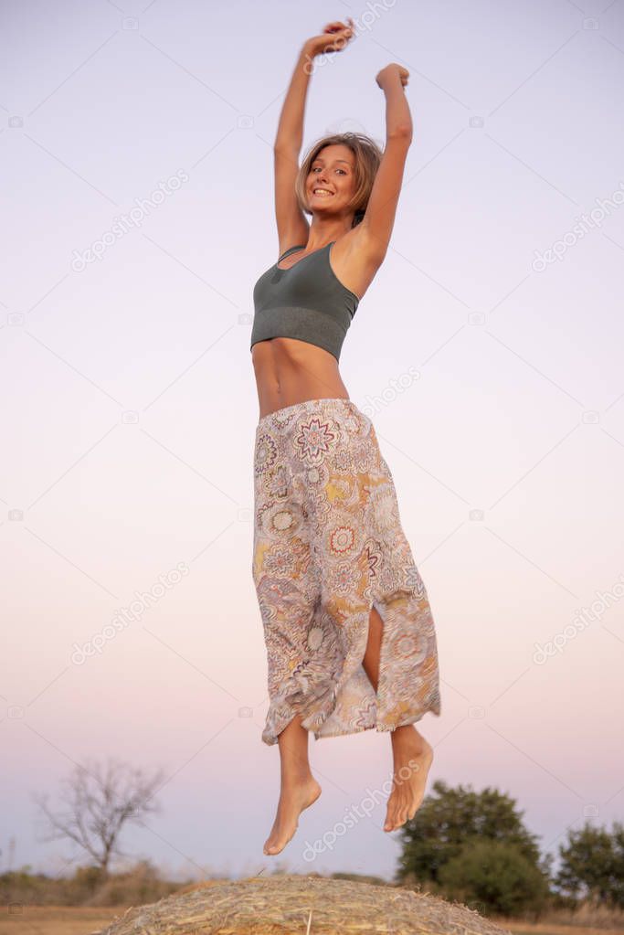 A beautiful, slender, smiling girl bounces on haystacks
