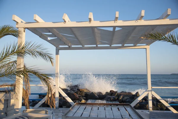 Varanda de madeira branca na praia. as ondas quebram nas rochas — Fotografia de Stock