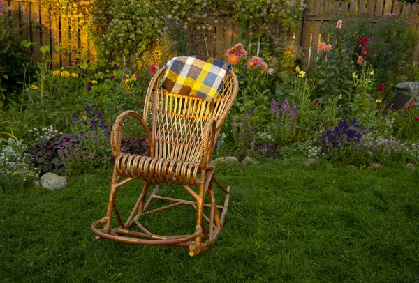 Uma cadeira de balanço de vime senta em um gramado em um jardim florescente — Fotografia de Stock