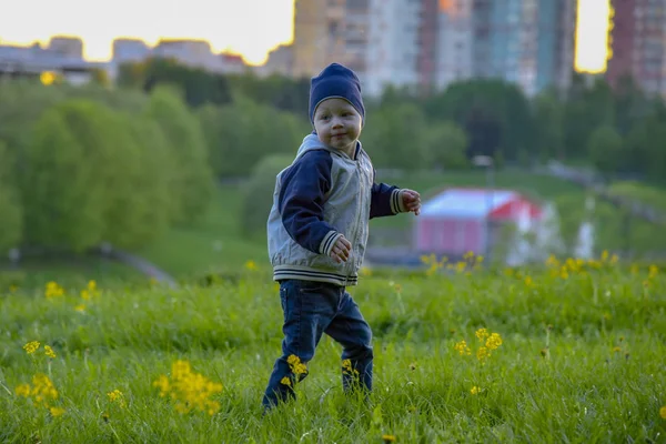 Маленький мальчик в шляпе бежит по зеленому лугу — стоковое фото