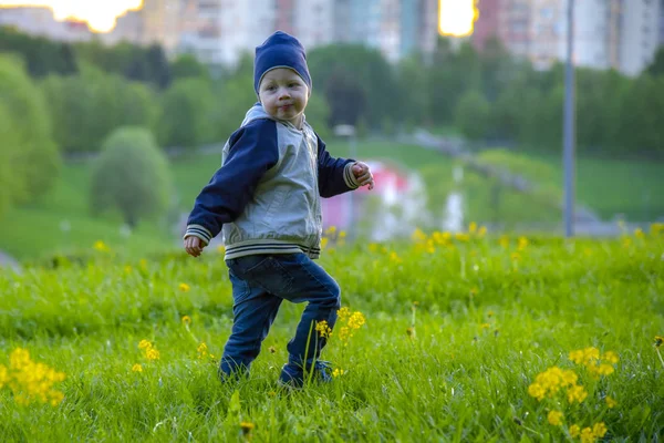 Маленький мальчик в шляпе бежит по зеленому лугу — стоковое фото