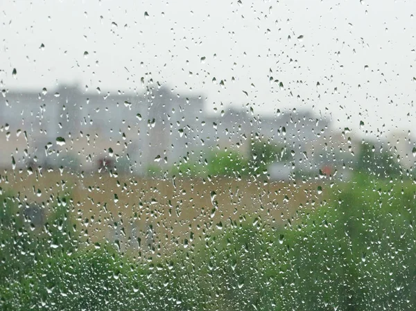 Vidrio de ventana con gotas de lluvia.Detrás del vidrio, casas borrosas —  Fotos de Stock