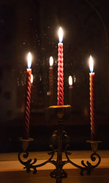 Ένα κηροπήγιο με τρία κόκκινα κεριά αξίζει στο περβάζι. Η φωτιά αντανακλάται στο γυαλί — Φωτογραφία Αρχείου