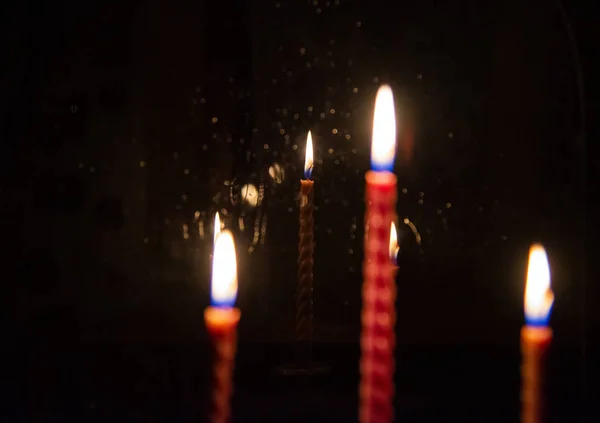 Op de voorgrond ongerichte drie brandende kaarsen. Ze worden weerspiegeld in het venster glas, — Stockfoto