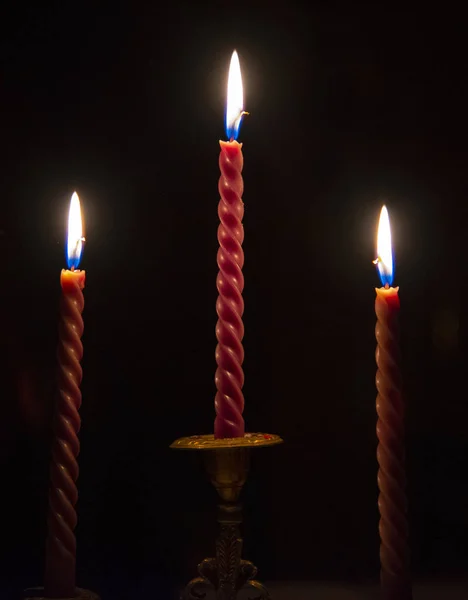 Tres velas rojas retorcidas encendidas en un candelero sobre un fondo oscuro . — Foto de Stock