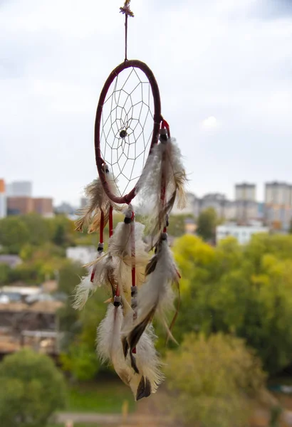 Pencereden asılı bir Dreamcatcher. Dışarıda, gökyüzü bulutlu ve şehir bulanık.. — Stok fotoğraf