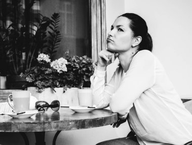 Bir kadın bir kafede bir masada oturur, masada iki fincan kahve. Siyah beyaz fotoğraf.