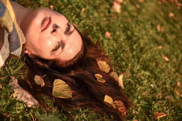A Portrait of a woman lying on the ground, autumn leaves scattered in her hair.