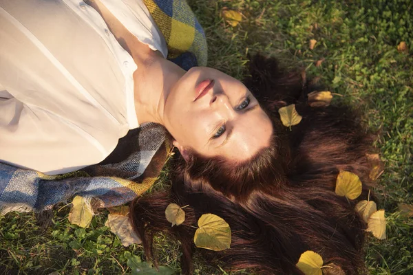 Een portret van een volwassen vrouw liggend op de grond, herfst bladeren verspreid in haar haar. — Stockfoto