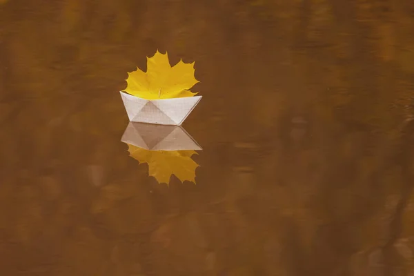 Een papieren boot drijft in een plas, een eiken rood blad in plaats van een zeil, rond de gevallen herfstbladeren liggen — Stockfoto