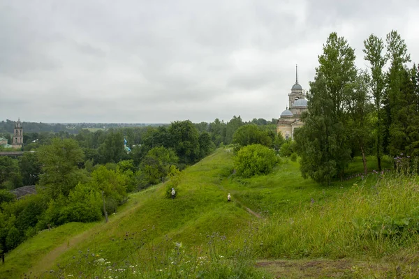 En kulle täckt med grönt gräs, en stig och en kyrka på toppen, gömd bakom träd. — Stockfoto