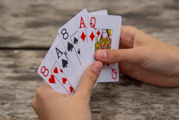 Playing cards in human hands on a wooden background.