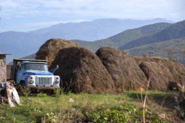 Büyük samanlıklar ve arka planda dağlar ve gökyüzünde bir kamyon..