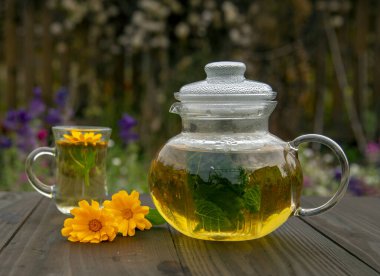 Şeffaf çaydanlık ve bulanık bir zemindeki ahşap masada bir fincan bitki çayı.