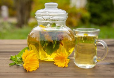 Şeffaf çaydanlık ve bulanık bir zemindeki ahşap masada bir fincan bitki çayı.