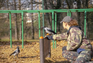 Köpeğin üstündeki Cynoloji uzmanı oyun parkı bir karga eğitiyor.