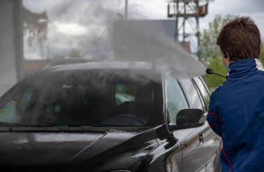Bir adam oto yıkamada araba yıkarken yüksek basınçlı araç yıkama makinesi köpük püskürtür..