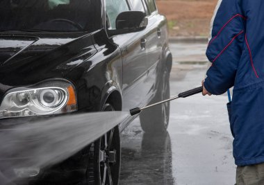 Bir adam oto yıkamada araba yıkarken yüksek basınçlı araç yıkama makinesi köpük püskürtür..