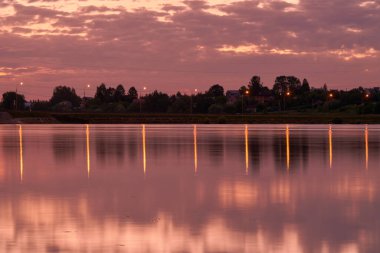 Uzun pozlama süresi olan bir fotoğraf. Parlak günbatımı ve fenerlerin ışığı gölün pürüzsüz suyuna yansıyor..