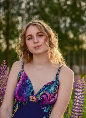 Doğanın arka planında uzun dalgalı saçları olan çekici sarışın bir kızın geniş dikey portresi..