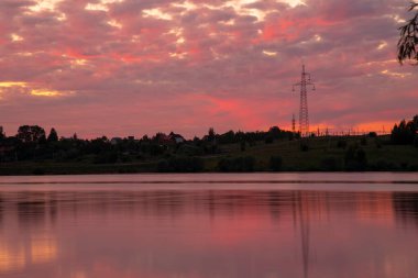 Gölün üzerinde parlak kırmızı bir günbatımı suya yansıyor. Fotoğraf uzun bir deklanşör hızı kullanılarak çekildi..