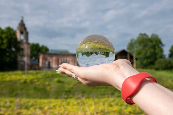 Glass ball in a woman\'s hand with a bright manicure.The old dilapidated Church is reflected in the lens.