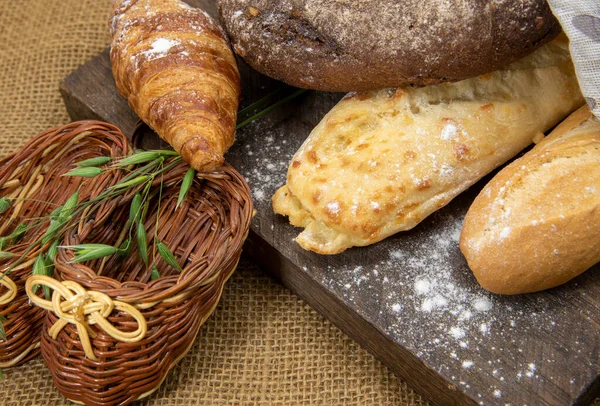 Paspaslamanın arka planına karşı kaba ahşap bir tahtanın üzerinde çeşitli ekmek türleri yatar. Fırın ürünleri reklam ediliyor, metin için alanı kopyala.