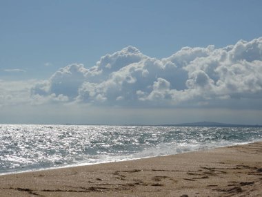 Boş bir kumsal ve bulutlu bir gökyüzünün altında köpüklü bir deniz. Deniz güneşin altında gümüş rengidir..